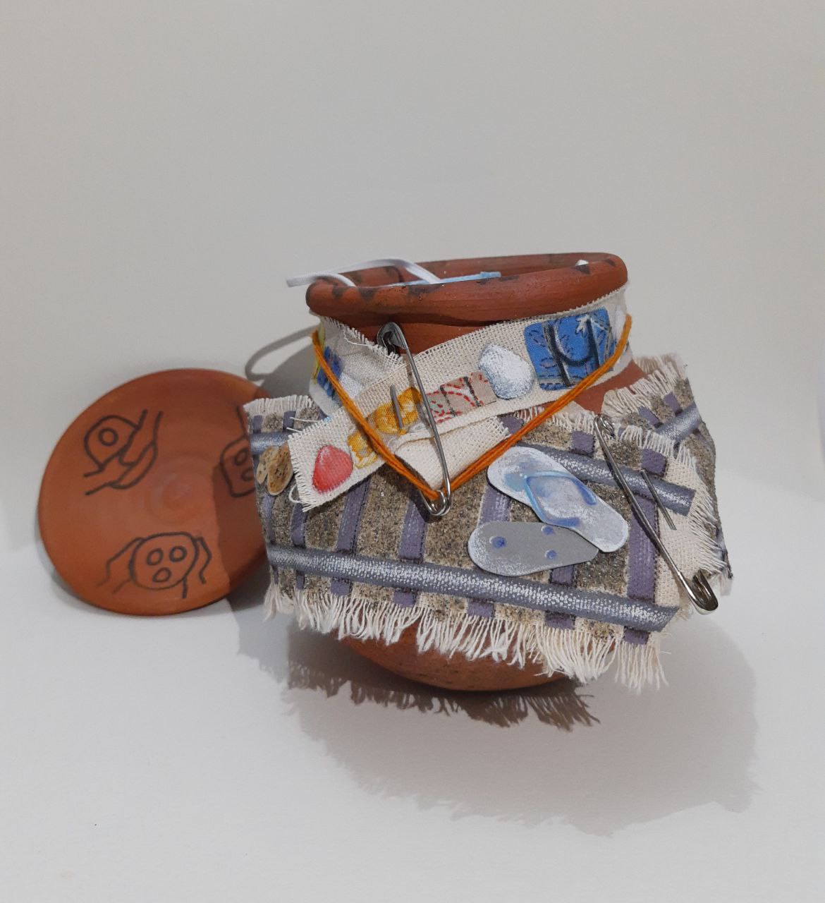 Terracotta pot decorated with beach-themed fabric scraps, safety pins, and small flip-flop appliqués.